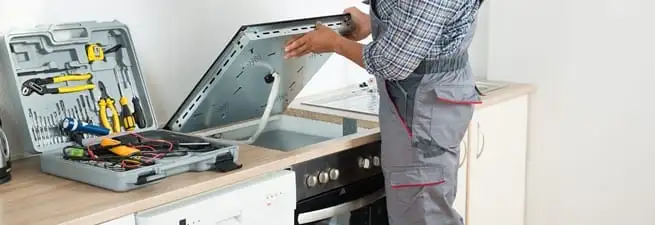 Cooktop repair technician lifting a built-in stovetop for service in San Francisco, CA