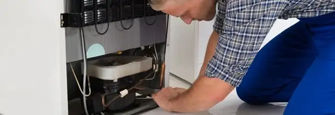 Refrigerator repair technician servicing the compressor and condenser area in San Francisco, CA