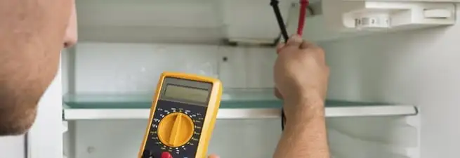 Refrigerator repair technician testing electrical components with a multimeter in San Francisco, CA