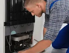 Refrigerator repair technician servicing the compressor and condenser area in San Francisco, CA
