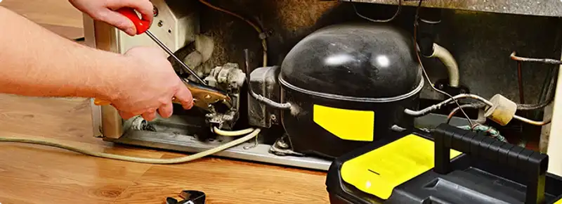 Refrigerator repair technician fixing the compressor and wiring in San Francisco, CA